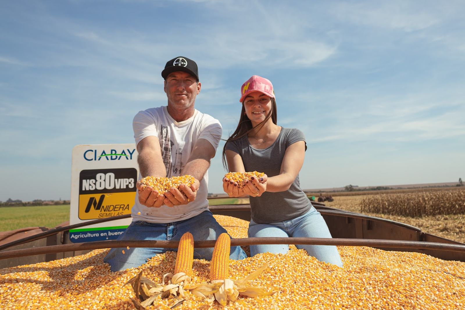 Productores mostrando granos de maíz NS 80 VIP 3 sobre la cosecha, junto al cartel CIABAY y Nidera Semillas