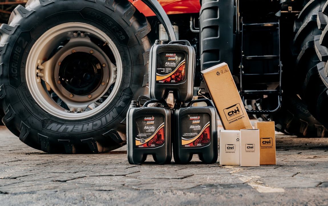 Bidones de lubricante Akcela de 20 litros junto a cajas CNH Genuine Parts frente a un tractor Case IH