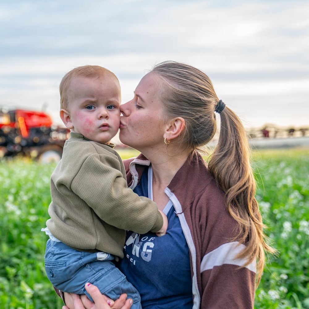 Madre con su hijo en brazos en el campo, con un pulverizador Case IH de fondo