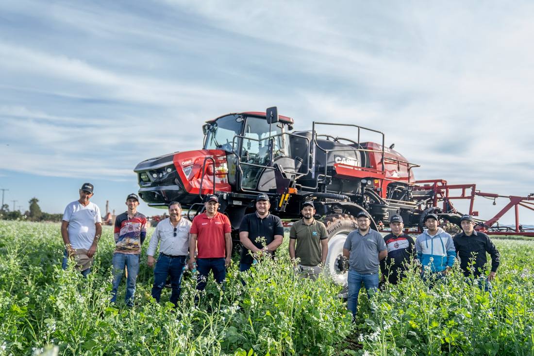 Grupo de técnicos y clientes frente al pulverizador Case IH Patriot en un campo de abono verde