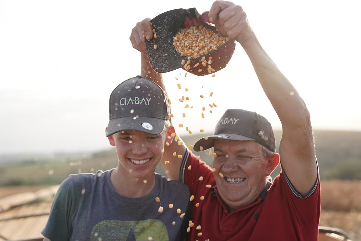 Padre e hijo con gorras CIABAY festejando la cosecha con granos de maíz cayendo
