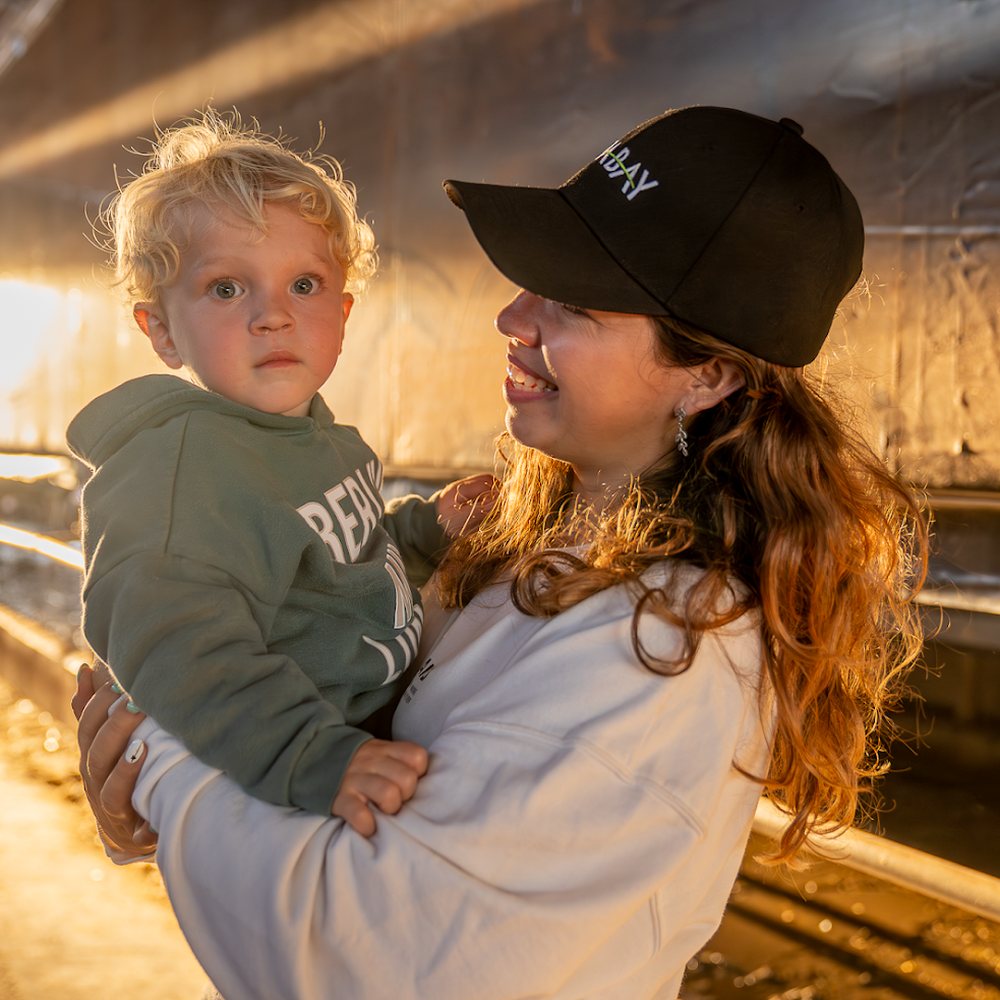 Madre con su hijo en brazos y gorra de CIABAY, en un galpón del campo con la luz del atardecer