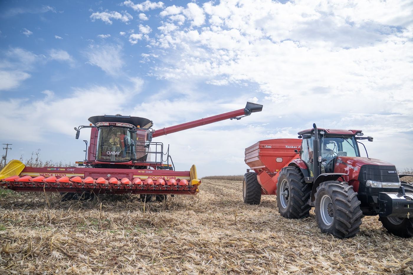 Cosechadora Case IH Axial-Flow con cabezal Vence Tudo Bocuda 7380 descargando maíz en una tolva junto a un tractor Puma